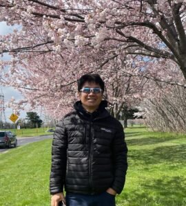 Person smiling under blooming cherry blossoms in park.