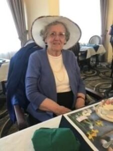 Elderly woman in hat at dining table.