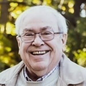 Smiling elderly man outdoors with greenery background.