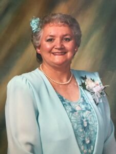 Smiling woman in blue dress with floral corsage.