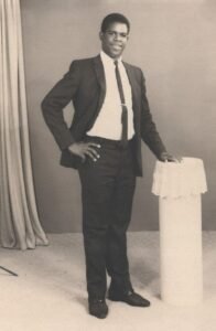 Man in suit posing next to decorative column.
