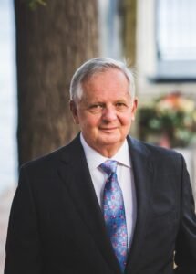Elderly man in suit smiling outdoors.