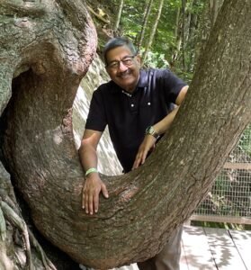 Smiling person posing with large curved tree.