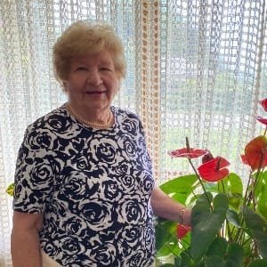 Smiling woman with anthurium plant indoors.