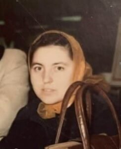 Person with a headscarf, seated indoors, carrying a bag.
