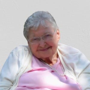 Smiling elderly woman in glasses and pink shirt.