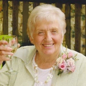Elderly woman smiling, holding glass of wine.