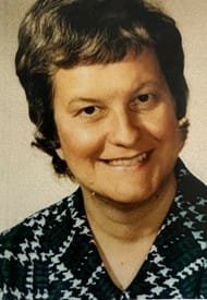 Smiling person with short hair and patterned shirt.