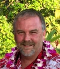 Smiling man wearing floral lei and colorful shirt.