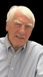 Elderly man smiling in a light blue shirt.