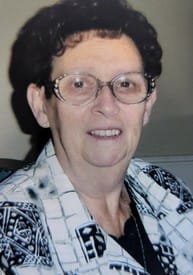 Smiling elderly woman wearing glasses and patterned shirt.