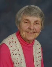 Smiling elderly woman in red sweater and vest.