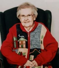 Elderly woman smiling in festive sweater.