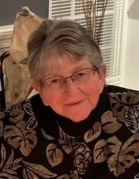 Elderly woman smiling wearing glasses and patterned sweater.