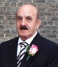 Man in suit with flower boutonniere, brick wall background.