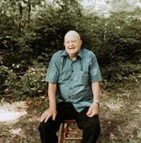 Elderly man sitting on stool in forest