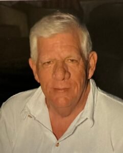 Elderly man with white hair, wearing a white shirt.