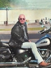 Person sitting on motorcycle near scenic background.