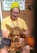 Man sitting with brown dog, pumpkin nearby.