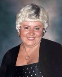 Smiling person with short white hair and black outfit.