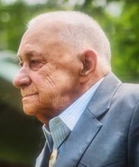 Elderly man in suit, outdoors, profile view.