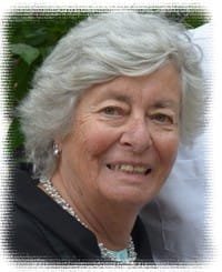 Elderly woman smiling with gray hair and pearls.