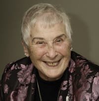 Smiling elderly person with short hair and floral jacket.