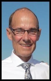 Smiling man wearing glasses and a tie outdoors.