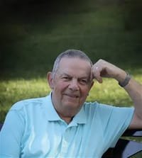 Smiling man sitting outdoors in blue shirt.