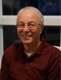 Smiling elderly man in maroon shirt indoors.