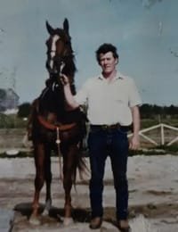 Man standing next to a brown horse outdoors.