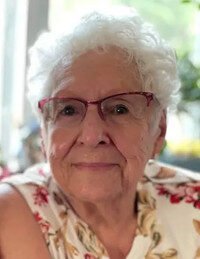 Elderly woman with white hair and glasses smiling.