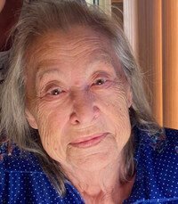 Elderly woman smiling indoors in blue blouse.