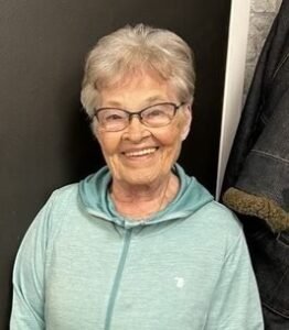 Smiling elderly woman wearing glasses and teal jacket.
