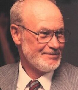 Elderly man in glasses with a beard smiling.