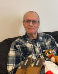 Man with glasses and plaid shirt sitting indoors.