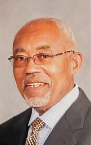 Elderly man smiling wearing glasses and suit