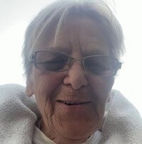 Elderly person wearing glasses smiling outdoors.