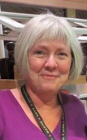 Smiling person with short gray hair indoors.