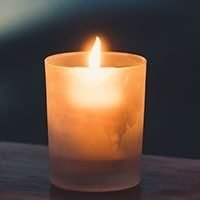 Lit candle in a glass holder on table.