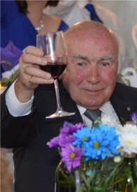 Elderly man toasting with red wine at event.