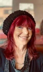 Smiling person with red hair and black hat.