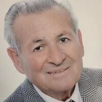 Elderly man smiling in a gray plaid suit.