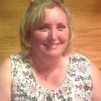 Smiling woman in floral top against wooden background.