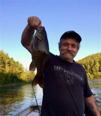 Man proudly holding a caught fish on river.