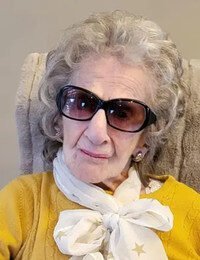 Elderly woman with sunglasses and white scarf.