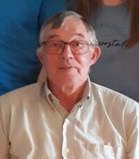 Elderly man wearing glasses and a light shirt.