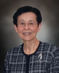 Smiling person in formal attire against dark background.