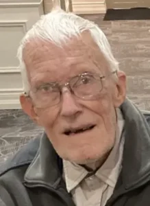 Elderly man with glasses smiling indoors.
