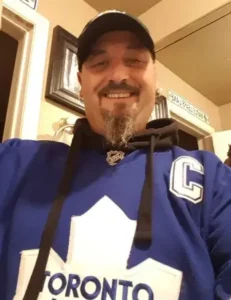 Smiling man wearing Toronto Maple Leafs jersey indoors.